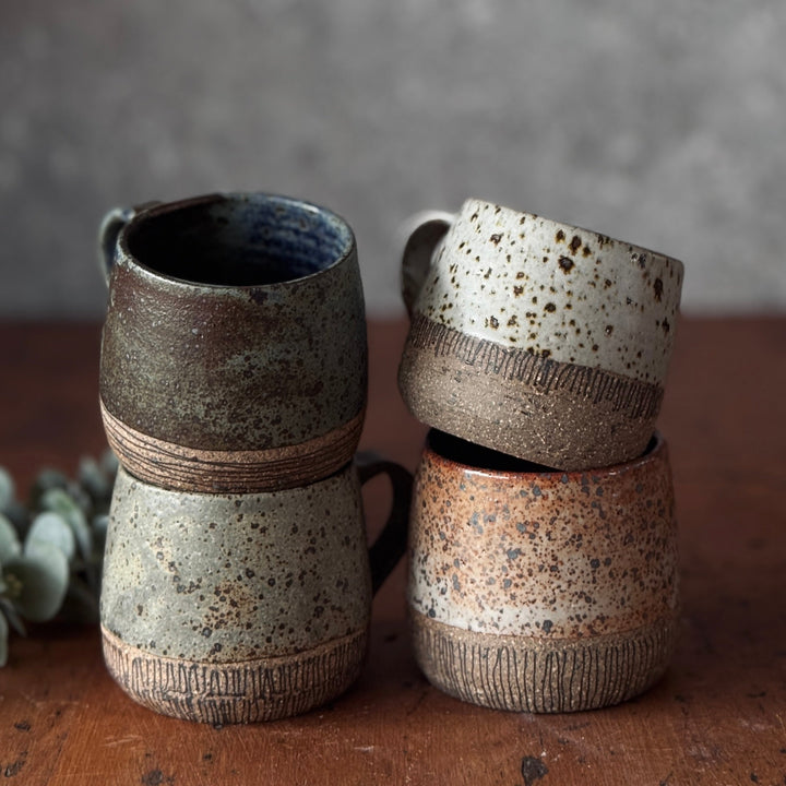 Three ceramic cups with speckled glaze on a wooden surface against a gray background