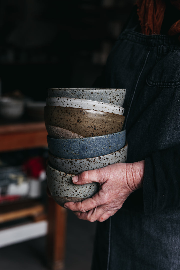 Person holding a stack of ceramic bowls with a dark background